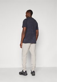 Mörkblå kortärmad T-shirt tillsammans med ljusgrå mjukisbyxor med en rand längs sidan, och svarta sportskor med vita detaljer.