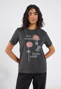 Svart bomulls t-shirt med blommönster i rosa och vitt, med texten "lev enkelt" och "blomstra vilt" tryckt i vitt.