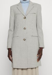 Rutig kavaj i grått och vitt med tre knappar, slagkrage och två framfickor. Bärs över en ljusblå polotröja.