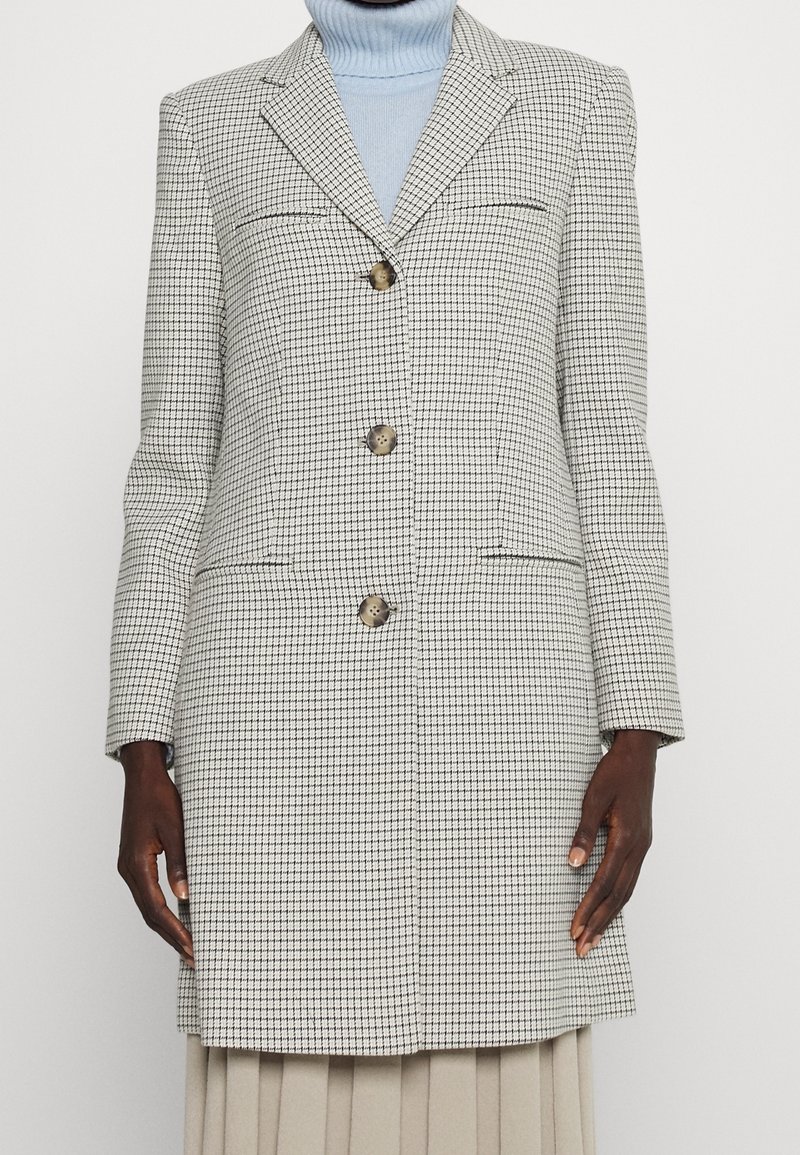 Rutig kavaj i grått och vitt med tre knappar, slagkrage och två framfickor. Bärs över en ljusblå polotröja.