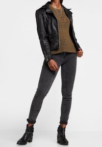 Schwarze Leder-Bikerjacke über einem grünen gestrickten Top, kombiniert mit grauen Skinny-Jeans und schwarzen Stiefeletten mit einem dicken Absatz.