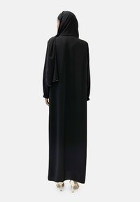 Musta'ab hitam lengan panjang dengan desain mengalir dan jilbab yang dililit. Tekstur mirip satin dengan aksen emas lembut di sepanjang lengan.
