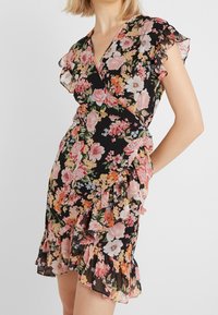 Robe fleurie avec un fond noir, manches volantes, design enroulé et ourlet à volants. Présente de grandes fleurs roses et blanches avec des accents verts.