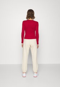 Top rojo de manga larga combinado con pantalones de chándal crema; la modelo lleva zapatillas blancas con acentos rosas. Diseño sencillo, textura suave, forma ajustada.