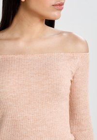 Hennon vaaleanpunainen, olkapäiden yli yltävä neulepaita, jossa on ribbikuviointi ja pitkät hihat. Neulepaita on muotoiltu istuvaksi ja siinä on hienovarainen kiilto.