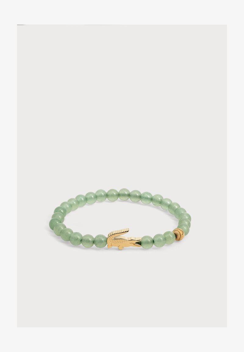 Bracelet vert à perles avec un pendentif en forme de crocodile doré et une petite perle dorée sur fond blanc.
