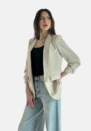 Beige satijnen blazer met een getailleerde pasvorm, opstaande revers en driekwart mouwen, gecombineerd met hoogzittende lichte denim jeans.