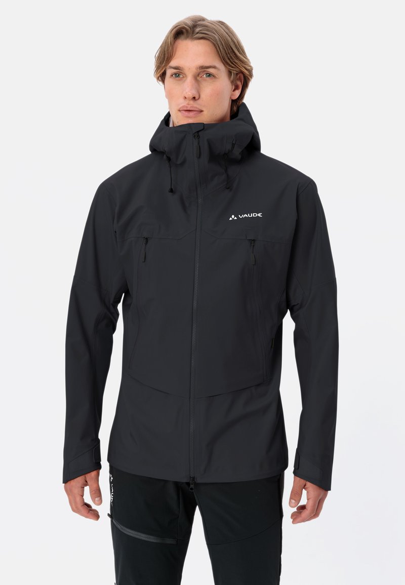 Giacca impermeabile nera con colletto alto, tasche frontali con zip, cappuccio regolabile e logo sul lato sinistro del petto. Texture liscia e opaca.