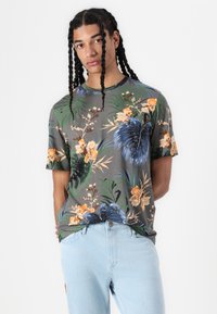 Grå kortermet t-skjorte med et blomstermønster i oransje, blått og grønt. Kombinert med lyseblå jeans. Myk stofftekstur.