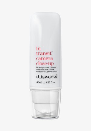 White cylindrical bottle with a pump, featuring black and red text. Product name: "in transit camera close-up," 40ml size indicated.