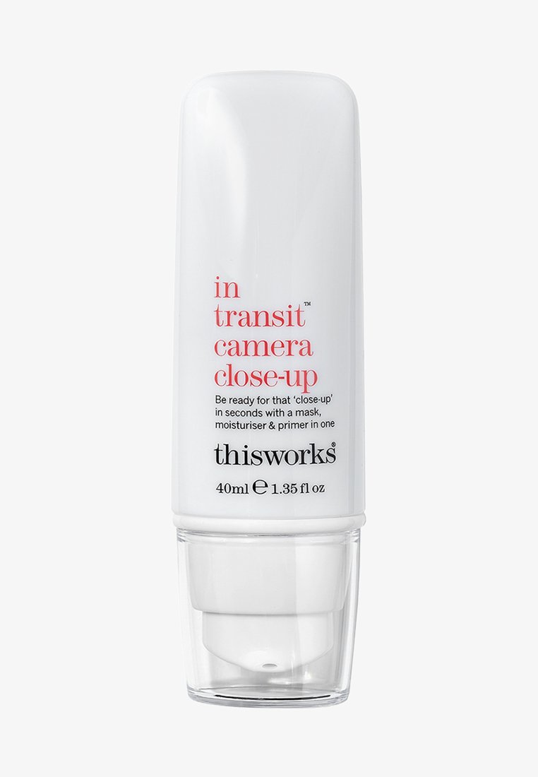 Bouteille cylindrique blanche avec un distributeur, comportant du texte noir et rouge. Nom du produit : "in transit camera close-up," taille indiquée de 40 ml.