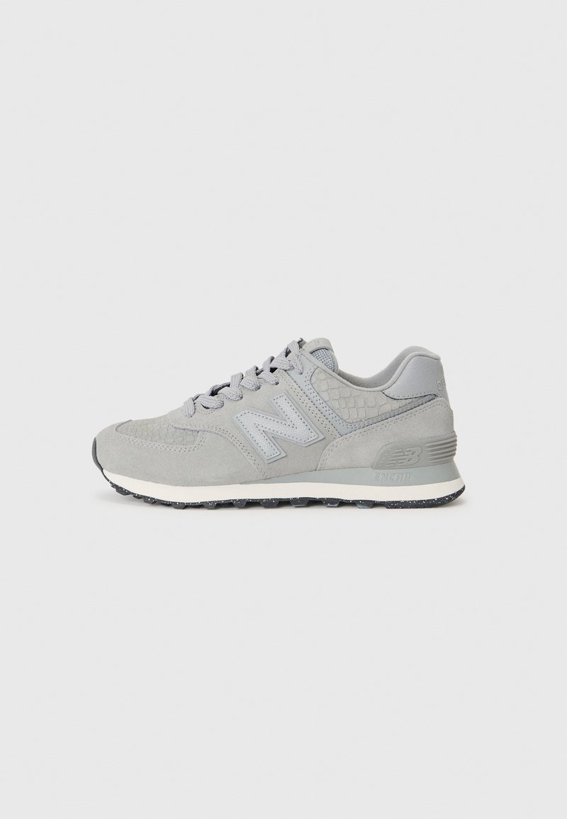 Baskets New Balance en suède et mesh gris avec lacets, détails texturés et semelle blanche sur fond uni gris clair.