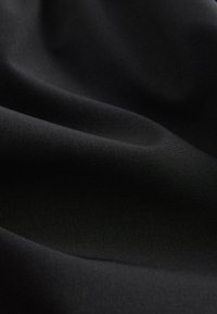 Tissu noir lisse avec des plis doux et une texture subtile, montrant des variations de lumière et d'ombre sur le matériau.