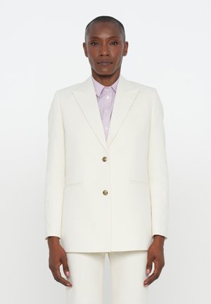 White tailored blazer with two buttons, a notched lapel, and side pockets. Worn over a light purple striped shirt. Textured fabric.
