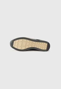 Semelle de sneaker noire en caoutchouc texturé pour une meilleure adhérence, avec une semelle intermédiaire beige et un motif géométrique. Bords lisses et design de bout arrondi.