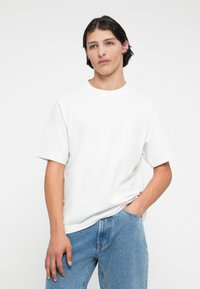 Valge puuvillane t-särk, millel on ümmargune kaelus ja lühikesed varrukad, koos siniste teksadega, millel on lõdva soe ja heledat toonist pesu.