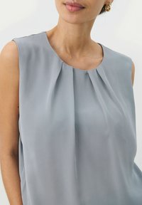 Light grey sleeveless blouse made of smooth fabric, featuring soft pleats at the neckline and a subtle drape, creating an elegant silhouette.