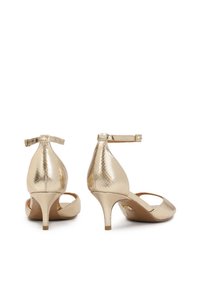 Escarpins en simili cuir doré avec une finition texturée, un bout pointu, une bride réglable à la cheville et un talon fin de 2,5 pouces.