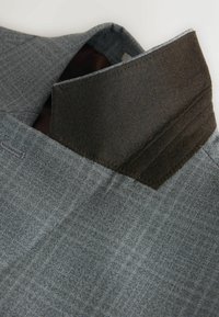 Grauer Stoff mit strukturierter Oberfläche, kontrastierendem dunklem Kragen und sauberer Naht entlang der Kanten.