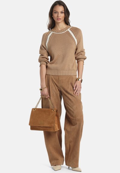 Pulover bej tricotat cu mâneci bufante, cusături albe de accent, asortat cu pantaloni largi din piele întoarsă de culoare tărtăcuță și o geantă maro din piele întoarsă cu lanț auriu.