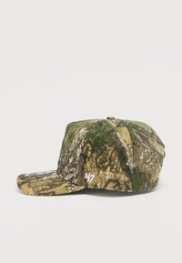 Καπέλο καμουφλάζ με δομημένο σχέδιο, πράσινα και καφέ μοτίβα που θυμίζουν φλοιό και φύλλωμα, με λευκό κεντημένο λογότυπο.