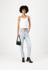 Bijeli rebrasti crop top s tankim naramenicama, svijetloplave traperice visokog struka, crne čizme na petu do članka i mala crna torba s logom.
