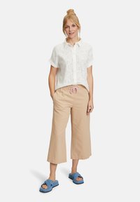 Witte, kortebloes met een textuurpatroon, gecombineerd met lichtbeige, loose-fitting broek met een roze trekkoord, en blauwe slippers.