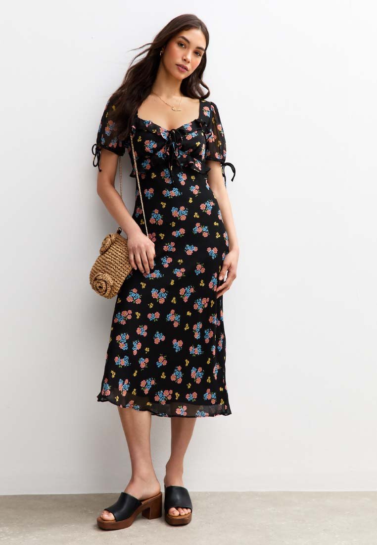 Robe midi noire à motifs floraux, avec des manches courtes bouffantes, un détail à nouer à l'avant et des motifs de fleurs colorées. Associée à des chaussures à plateforme noires.