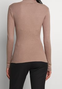 Ribattu turtleneck-sweater vaaleanruskeana, jossa on tiivis malli, pitkät hihat ja vastakkaiset hihansuut. Pehmeä rakenne, jossa on hieno venyvyys.