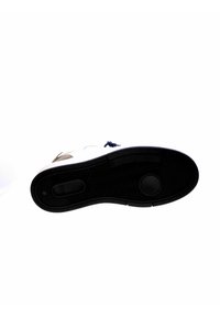 Suola di sneaker bianca con suola in gomma nera. Presenta un motivo di presa testurizzato, indentazioni circolari e un rinforzo per il tallone per un supporto aggiuntivo.