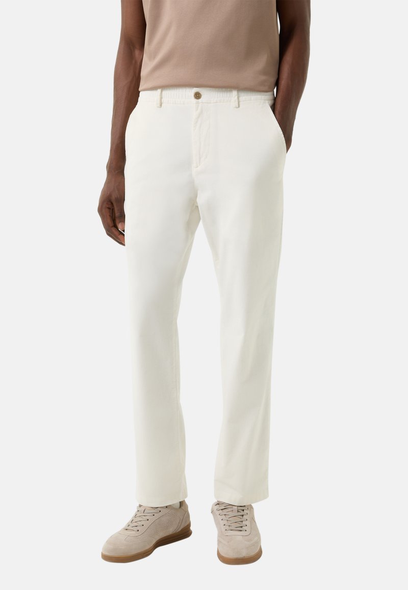 Białe bawełniane spodnie o luźnym kroju, z zapięciem na guzik i bocznymi kieszeniami. Do tego beżowe sneakersy na sznurowadła.