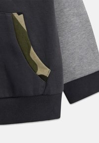 Tissu de sweatshirt gris foncé et gris clair avec une poche à motif camouflage et des poignets côtelés, offrant une texture lisse et un design sportif.