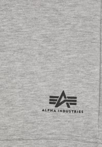Siva majica iz mehkega materiala, z črnim grafičnim logotipom in stiliziranimi črkami ter črtami blizu spodnjega roba.