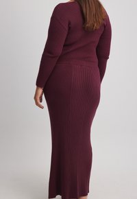 Långt ribbat klänning i mörk burgundy med långa ärmar. Smal passform, rundad halsringning och knälång nederdel. Mjuk, texturerad stickad material.