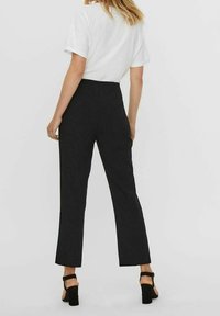 Pantalones negros ajustados con un diseño de pierna recta, cintura alta y tejido suave. Combinados con una camiseta blanca de cuello redondo y sandalias de tacón cuadrado.