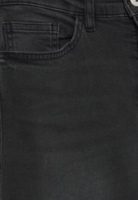 Zbliżenie czarnych dżinsów z denimu pokazujące przednią kieszeń, małą kieszonkę na monety, szlufkę na pasek oraz metalowy guzik.