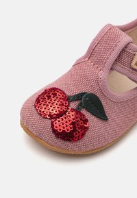 Rozā auduma kurpe ar teksturētu virsmu, kas rotāta ar sarkanu spīguļojošu ķiršu dizainu un zaļiem lapu akcentiem uz pirksta. Velcro siksna drošai piegulšanai.