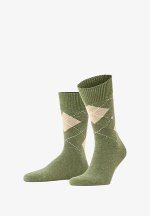 Grüne Socken mit einem gerippten oberen Teil, ausgestattet mit einem Rautenmuster in Creme und einer strukturierten Oberfläche. Entwickelt für Komfort und Wärme.