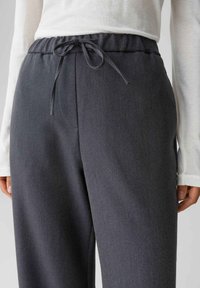 Grijze broek met elastische taille en trekkoord. De stof heeft een gestructureerde weving, het ontwerp heeft een ontspannen pasvorm en zijszakken.