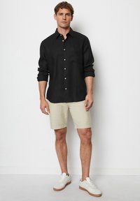 Zwarte lange-vingerknopshirt van linnen, gecombineerd met lichtbeige shorts en witte sneakers met bruine zolen. Eenvoudig ontwerp en pasvorm.