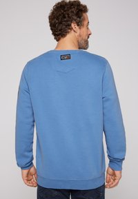 Felpa azzurra chiara con maniche lunghe, polsini e orlo a coste. Presenta un piccolo etichetta con il marchio sul retro del collo, texture di cotone liscia.