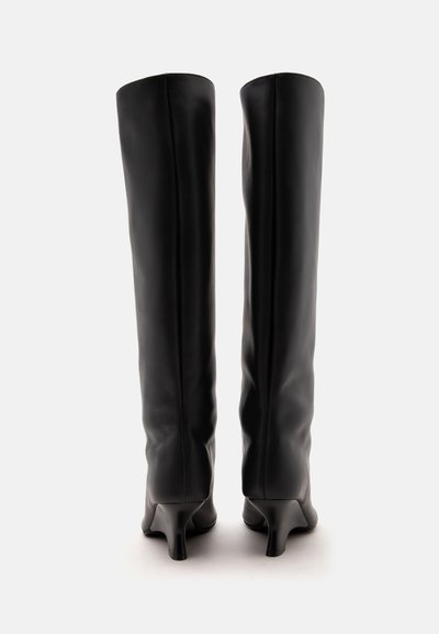 Paire de bottes en cuir noir montant jusqu’aux genoux avec des petits talons étroits, vues de dos sur fond blanc.