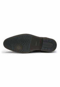 Sole in gomma nera con grip testurizzato, caratterizzata da un emblema circolare e motivi rigati per una maggiore trazione. Design piatto e arrotondato.