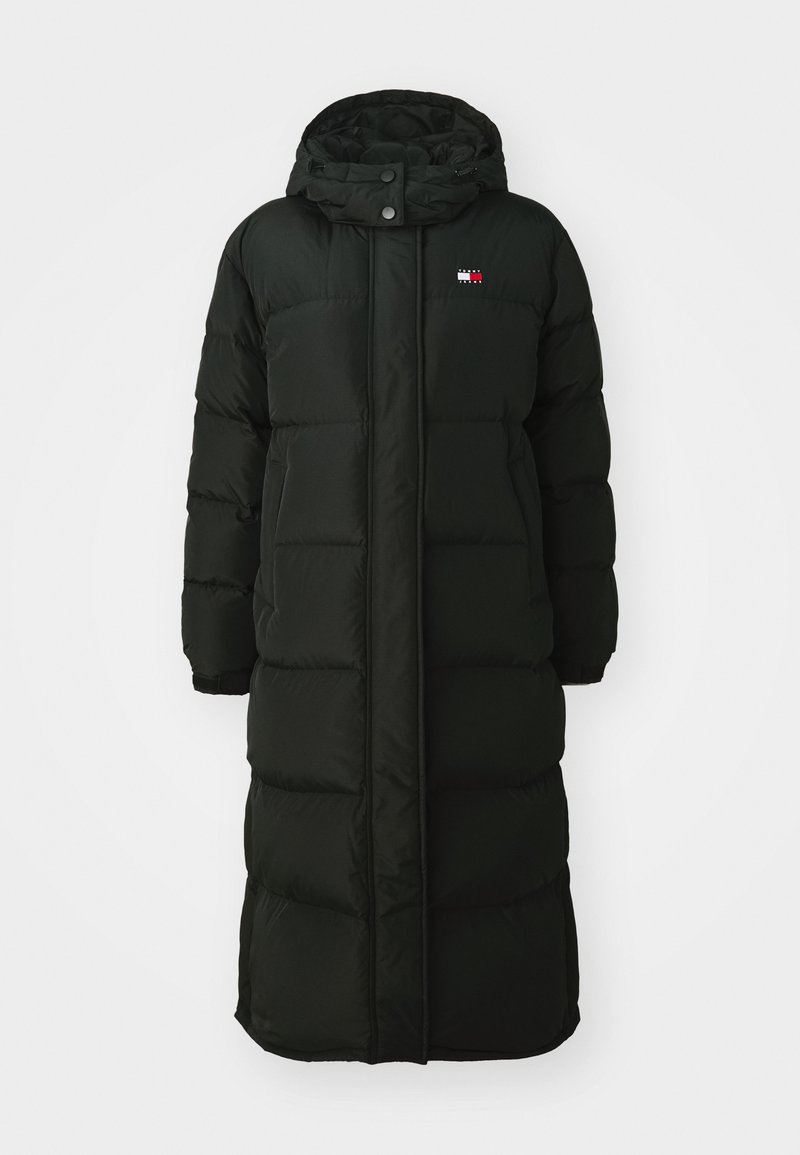 Langer schwarzer Puffer-Mantel mit Kapuze, ausgestattet mit einem Frontreißverschluss und Druckknöpfen. Er hat eine gesteppten Textur und ein kleines Logo auf der Brust.