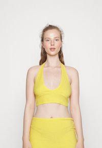 Top cropped amarelo em halter, feito de um tecido suave, com um decote em V profundo e uma silhueta ajustada. Textura lisa sem padrões visíveis.