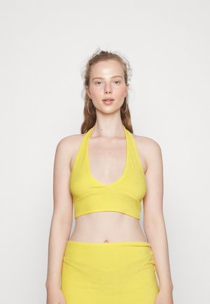 Top cropped amarelo em halter, feito de um tecido suave, com um decote em V profundo e uma silhueta ajustada. Textura lisa sem padrões visíveis.