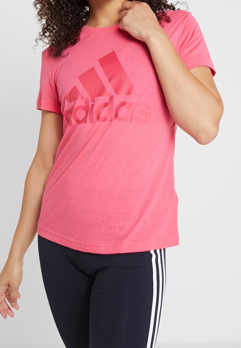 Camiseta rosa de Adidas con cuello redondo y mangas cortas, con un gran logo en un tono ligeramente más oscuro, confeccionada con una tela suave y ligera.