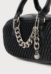 Crna kviltana kožna torba s debelom srebrnom lancem i okruglim srebrnim privjeskom pričvršćenim za ručke.