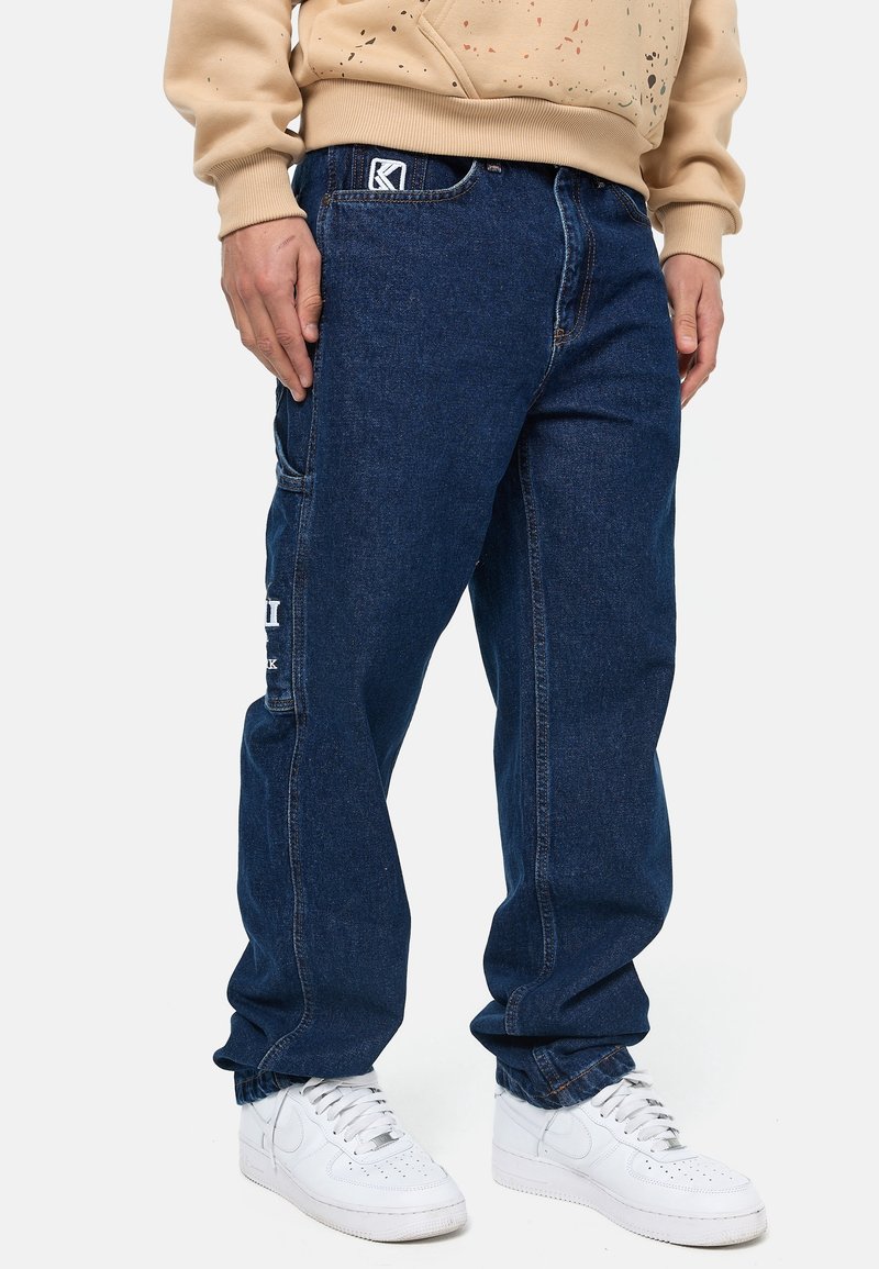 Blå denim-joggers med en avslappnad passform, med en logotyp på framsidan, sidofickor och uppvikta fållar. Matchas med vita sneakers.