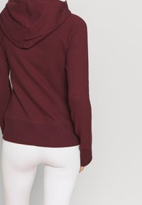 Bordeaux hoodie med en tekstureret overflade, lange ærmer og skjortetræk, som har en ensfarvet farve og ribbet kant.